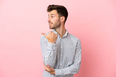 Pembe arka planda izole edilmiş beyaz, yakışıklı genç bir adam bir ürün sunmak için kenarı işaret ediyor.