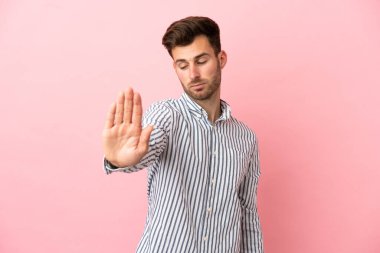 Pembe arka planda izole edilmiş beyaz, yakışıklı genç adam dur hareketi yapıyor ve hayal kırıklığına uğruyor.