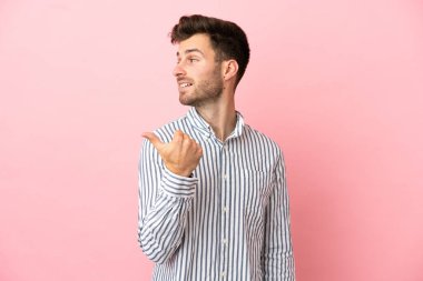 Pembe arka planda izole edilmiş beyaz, yakışıklı genç bir adam bir ürün sunmak için kenarı işaret ediyor.