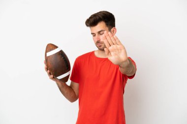 Beyaz arka planda ragbi oynayan beyaz bir adam durdurma hareketi yapıyor ve hayal kırıklığına uğruyor.