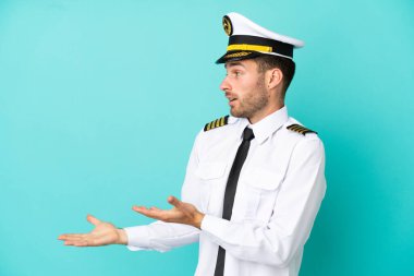 Kafkasyalı uçak pilotu mavi arka planda şaşırmış bir yüz ifadesiyle izole edildi.