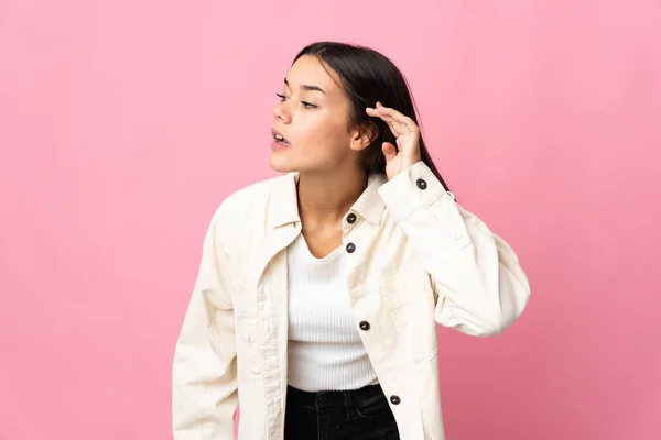 Nastolatka Odizolowana Różowym Tle Słuchając Czegoś Kładąc Rękę Uchu — Zdjęcie stockowe