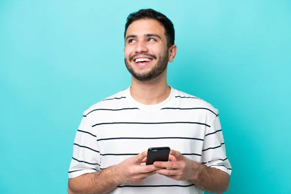 Νεαρός Βραζιλιάνος Απομονωμένος Μπλε Φόντο Χρησιμοποιώντας Κινητό Τηλέφωνο Και Κοιτάζοντας — Φωτογραφία Αρχείου