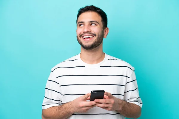 Junger Brasilianer Isoliert Auf Blauem Hintergrund Mit Handy Und Blick — Stockfoto