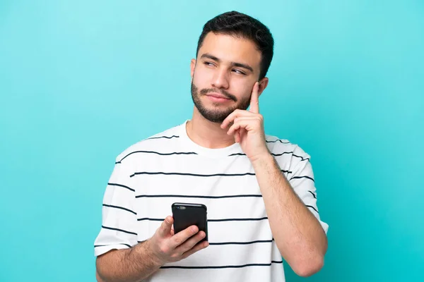 Νεαρός Βραζιλιάνος Απομονωμένος Μπλε Φόντο Χρησιμοποιώντας Κινητό Τηλέφωνο Και Σκέψη — Φωτογραφία Αρχείου