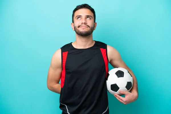 Młody Piłkarz Brazylijczyk Człowiek Odizolowany Niebieskim Tle Patrząc Górę — Zdjęcie stockowe