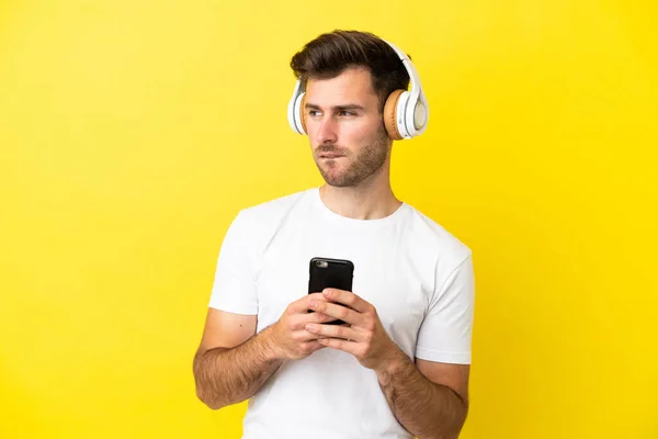 Joven Hombre Guapo Caucásico Aislado Sobre Fondo Amarillo Escuchando Música —  Fotos de Stock