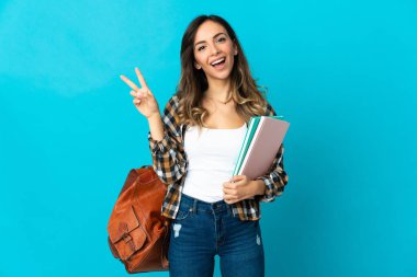 Mavi arka planda izole genç bayan gülümseyerek ve zafer işareti göstererek