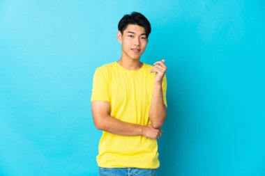 Genç Çinli adam mavi arka planda yalnız gülüyor.