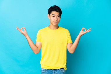 Zen pozisyonunda mavi arka planda izole edilmiş genç bir Çinli.