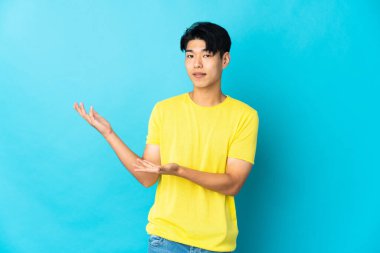 Mavi arka planda izole edilmiş genç bir Çinli davet etmek için ellerini yana uzatıyor.
