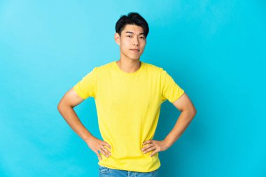 Genç Çinli adam mavi arka planda izole edilmiş kızgın.