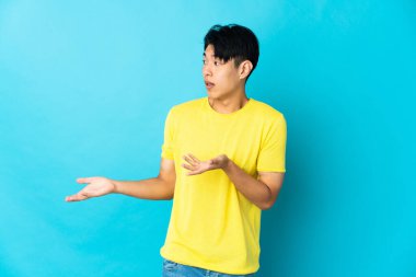 Mavi arka planda mahsur kalmış genç Çinli bir adam sürpriz bir ifadeyle yan tarafa bakıyor.