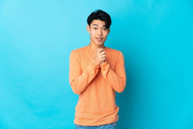 Genç Çinli adam mavi arka planda yalnız gülüyor.