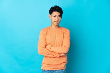 Mavi arka planda, mutsuz bir ifadeyle izole edilmiş genç bir Çinli.
