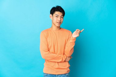 Mavi arka planda izole edilmiş genç bir Çinli mutlu ve dik duruyor.