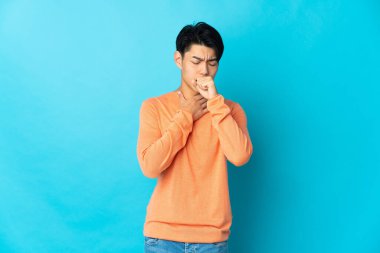 Genç Çinli adam mavi arka planda izole edilmiş, çok öksürüyor.