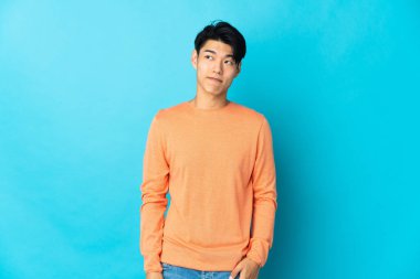 Genç Çinli bir adam mavi arka planda izole edildi.