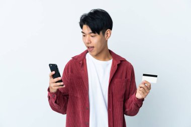 Genç Çinli bir adam beyaz arka planda izole edilmiş cep telefonuyla kredi kartıyla alışveriş yapıyor.