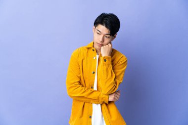 Genç Çinli adam mor arka planda izole edilmiş, yorgun ve sıkılmış bir ifadeyle.