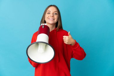 Genç Litvanyalı bir kadın mavi arka planda izole edilmiş. Elinde baş parmağıyla bir megafon tutuyor.