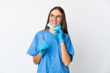 Litvanyalı kadın diş hekimi, arka planda izole edilmiş araçları tutarken bir yandan düşünürken, bir yandan da