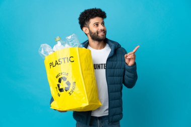 Genç Faslı bir adam, izole edilmiş arka planı geri dönüştürmek için plastik şişelerle dolu bir çanta tutuyor.