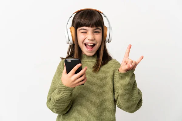 小さな女の子リッスン音楽とともにモバイル隔離されたオンホワイトバックリスニング音楽とともにAモバイルメイキングロックジェスチャー — ストック写真