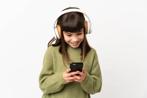 小さな女の子リッスン音楽とともにモバイル孤立した上に白い背景リスニング音楽と見ますモバイル — ストック写真