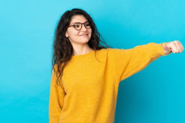 Genç Rus kız, mavi arka planda izole edilmiş bir şekilde baş parmak işareti yapıyor.