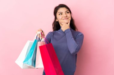 Pembe arka planda izole edilmiş genç Rus kız elinde poşetler ve düşünüyor.