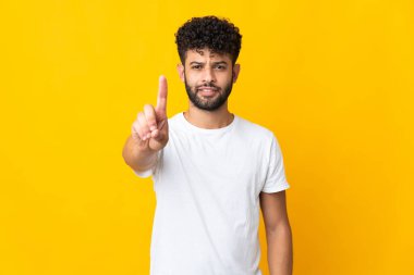 Sarı arka planda izole edilmiş genç Faslı adam ciddi bir ifadeye sahip birini sayıyor.