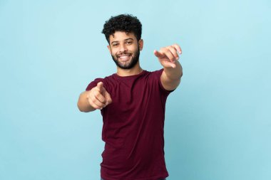 Mavi arka planda izole edilmiş genç Faslı adam mutlu bir ifadeyle cepheyi işaret ediyor.