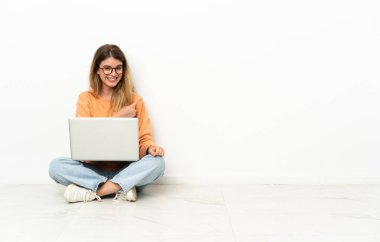 Dizüstü bilgisayarı olan genç bir kadın ürününü sunmak için yan tarafa bakıyor.