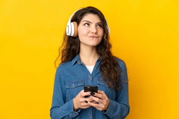 俄罗斯少女被隔离在黄色背景下 一边听音乐一边用手机思考 — 图库照片