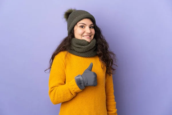 俄罗斯少女 头戴紫色背景的冬帽 竖起大拇指 — 图库照片