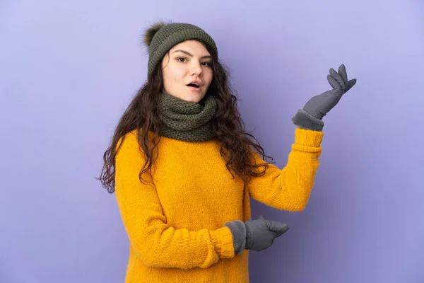 俄罗斯少女 头戴紫色背景的冬帽 向旁边伸出手来 邀请她来 — 图库照片