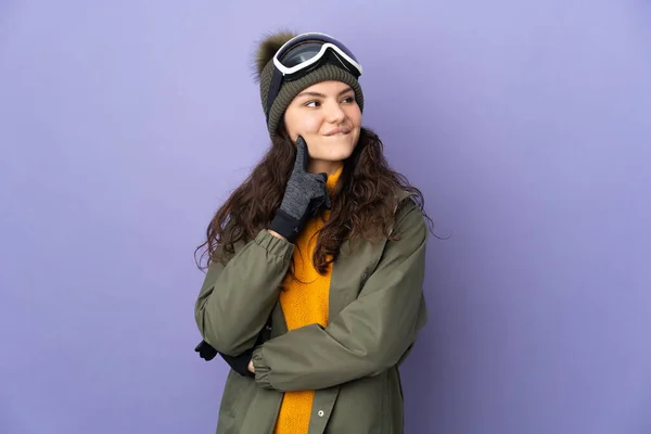 年轻的俄罗斯姑娘 戴着雪板眼镜 背景是紫色的 她抬头一看就想出了个主意 — 图库照片
