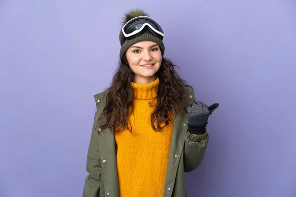 俄罗斯少女 戴着雪板眼镜 与紫色背景隔离 指向侧面来展示一种产品 — 图库照片