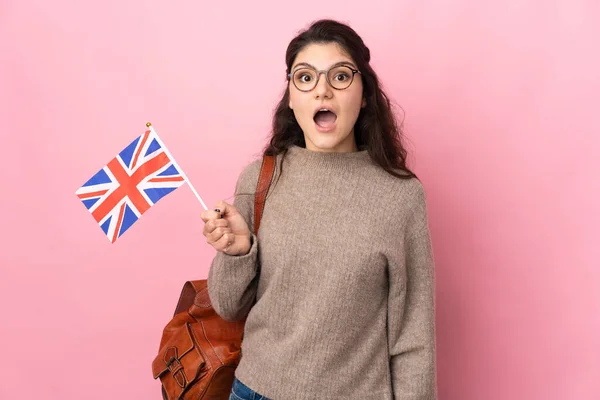 俄罗斯年轻女子手持英国国旗 背景为粉色 面部表情令人惊讶 — 图库照片