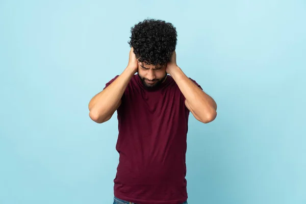 Young Moroccan man isolated on blue background frustrated and covering ears