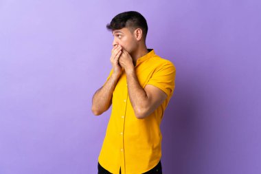 Genç Kolombiyalı adam mor arka planda izole edilmiş ağzını kapatıyor ve yan tarafa bakıyor.
