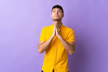 Mor arka planda izole genç Kolombiyalı adam avuç içlerini bir arada tutuyor. İnsan bir şey ister.