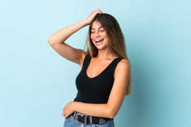 Mavi arka planda izole edilmiş genç beyaz kadın çok gülümsüyor.