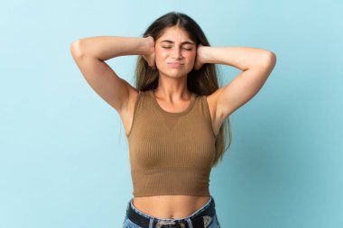 Mavi arka planda izole edilmiş genç beyaz kadın hayal kırıklığına uğramış ve kulaklarını kapatmış.