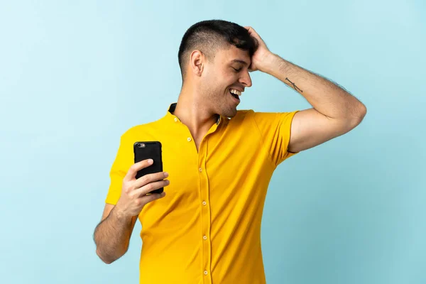 Молодий Колумбійський Чоловік Який Користується Мобільним Телефоном Ізольованим Синім Фоном — стокове фото