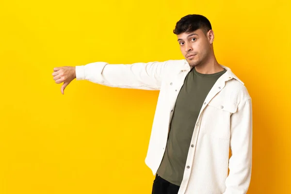 黄色の背景に孤立した若いコロンビア人男性は否定的な表現で親指を下に示す — ストック写真