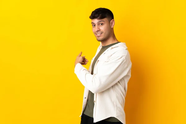 Sarı Arka Planda Izole Genç Kolombiyalı Adam Geriye Doğru Işaret — Stok fotoğraf