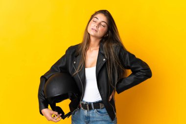 Sarı arka planda motosiklet kaskı tutan kadın çaba sarf ettiği için sırt ağrısı çekiyor.