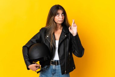 Sarı arka planda izole edilmiş motosiklet kaskı tutan ve şans dileyen bir kadın.